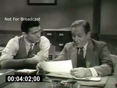 The still from 'Bell System - Story Without End' features two men sitting at a table in an office setting. One man, dressed in a vest and shirt, appears engaged in conversation, leaning in towards the other man, who is reading a document. The second man is dressed in a suit and tie, looking thoughtfully at the paper. The atmosphere seems professional, likely highlighting a discussion related to business or telecommunications. The time stamp indicates a moment from the film, while the 'Not For Broadcast' label suggests it's for archival purposes.