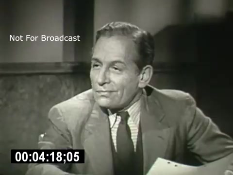 The still features a well-dressed man with a confident expression, seated at a table with papers in front of him. The setting appears to be a formal office or interview space, likely conveying a serious conversation. The timestamp suggests it is from a scene approximately four minutes and eighteen seconds into the film. The text 'Not For Broadcast' indicates that this image is intended for internal use only, not public distribution.