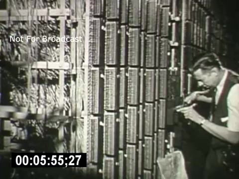 The still from *Bell System - Story Without End* shows a technician working on a complex network of telephone equipment. He is focused on adjusting or repairing a panel filled with rows of connectors or circuits, likely in a central office or switching facility. The scene highlights the technical expertise involved in maintaining telecommunications infrastructure. The timecode at the bottom indicates the video's elapsed time.