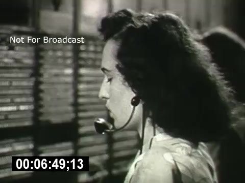 The still features a woman wearing a vintage headset, likely a telephone operator. She is focused, with her profile visible, as she interacts with a large panel of telephone switches behind her. The scene captures a moment of communication in a historical context, showcasing the technology and workforce of the Bell System era. A timestamp is visible at the bottom, indicating the duration of the clip. The label 'Not For Broadcast' suggests this is a restricted or archival still.