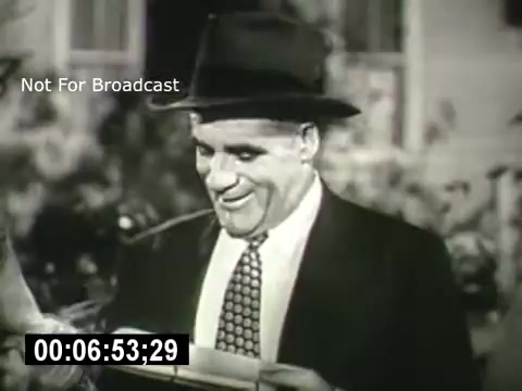 The still from 'Bell System - Story Without End' features a man in a suit and hat, smiling as he interacts with something in his hands. The scene conveys a sense of lightheartedness, likely reflecting a moment of joy or satisfaction. The black-and-white aesthetic adds a classic, vintage feel to the imagery.