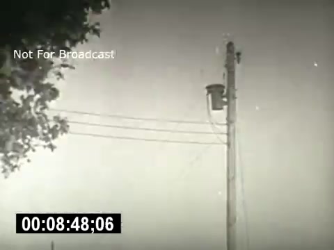 The still from 'Bell System - Story Without End' features a tall utility pole with wires attached, set against a cloudy sky. The frame captures an industrial scene typical of mid-20th century American telecommunications, emphasizing the infrastructure that supports communication systems. The timestamp indicates a moment in the film, highlighting its historical context.