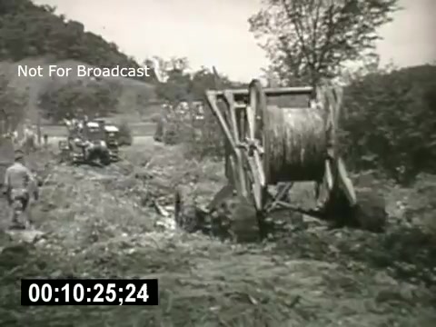 The still from 'Bell System - Story Without End' features a scene depicting the construction or maintenance of telephone lines. A large spool or reel is prominently displayed, possibly used for wiring, with workers seen nearby. The background includes a rural landscape, suggesting the film's focus on telecommunication infrastructure development in less urban areas.