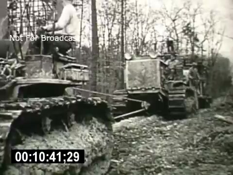 The still depicts two heavy machinery vehicles, likely bulldozers, at work in a forested area. A worker is seen riding on one of the machines while the other vehicle appears to be preparing the ground. This scene emphasizes industriousness and the transformative impact of technology on the landscape, fitting the narrative of the Bell System's exploration of progress and innovation.