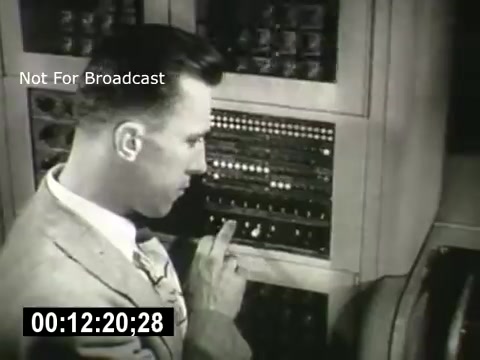 The still shows a man in a suit, focused on operating a vintage telephone switchboard. He has neatly styled hair and is adjusting a panel filled with buttons and lights. The setting appears to be a mid-20th century telecommunications environment, indicative of Bell System's operations. The timestamp suggests it's a moment captured from a longer film, and the watermark indicates it is not for broadcast.