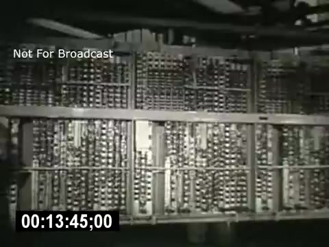 The still from 'Bell System - Story Without End' features a close-up view of a complex set of telephone switchgear. The image shows extensive rows of metallic components, likely relays and circuit connections, indicating the intricate technology behind telephone systems. It captures the scale and sophistication of telecommunications infrastructure during the time. The timecode in the corner shows it's part of an ongoing sequence, emphasizing its context within the larger narrative of the film.
