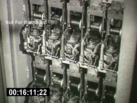 The still features a close-up of intricate mechanical components, likely part of a telephone switching system. It showcases a series of metal gears and levers, emphasizing the complexity of early telecommunications technology. The visual highlights the industrial design and engineering of the Bell System, likely used to illustrate advancements in communication infrastructure. The timecode at the bottom indicates the moment within the film.