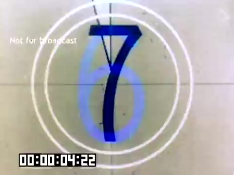 The still depicts a countdown timer from a 16mm film, featuring a large blue number '7' against a light background, surrounded by concentric circular graphics. It indicates that the film is about to start, with a digital timestamp reading '00:00:04:22.' There is also a 'Not for broadcast' watermark in the corner, suggesting the film is not intended for public viewing. This context relates to a silent Kodak sales film from 1977.