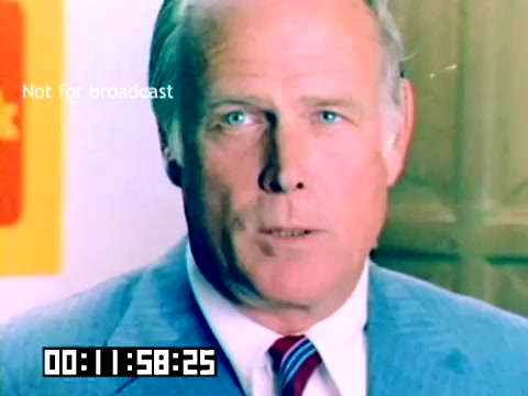 The still from the silent Kodak sales film features a gentleman in a light blue suit with a red and white striped tie, directly addressing the camera. He has short, neatly styled hair and bright blue eyes, exuding a confident demeanor. The background includes a Kodak logo, indicating the promotional nature of the film. The timestamp at the bottom suggests its position within the film. The overall aesthetic reflects the color and style typical of the late 1970s.