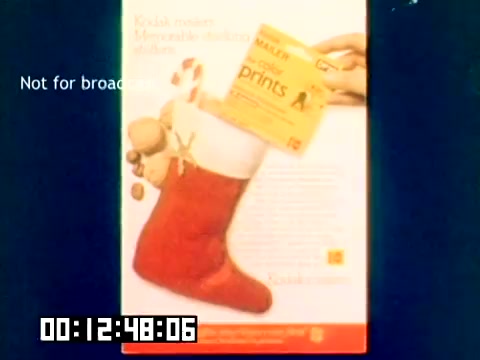 The still depicts a promotional advertisement for Kodak featuring a red Christmas stocking, with items like candy and a Kodak prints envelope spilling out. The ad emphasizes Kodak's focus on memorable moments and holiday themes. The lower part of the image displays a timer indicating the elapsed duration of the clip. The text 'Not for broadcast' is overlayed, signifying it's for internal use only. The overall tone is festive and marketing-oriented.