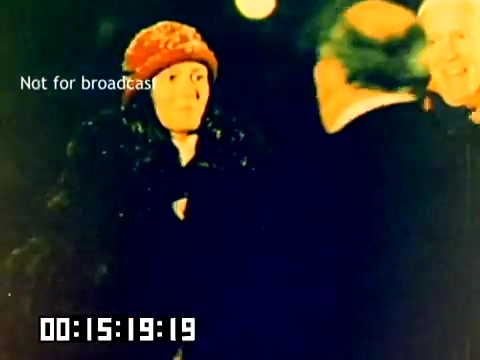 The still depicts a group of individuals, including a woman wearing a distinctive orange hat and curly hair, engaged in a casual outdoor setting. The lighting suggests it might be evening, with warm hues imparting a nostalgic feel typical of the 1970s. The text 'Not for broadcast' indicates the film's exclusivity, while the timestamp on the bottom captures the moment within the silent Kodak sales film from 1977. The ambiance hints at a cheerful or friendly interaction among the participants.