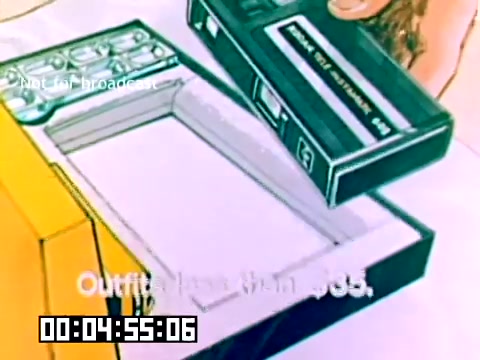 The still from the 1977 Kodak sales film shows a hand holding a cassette tape, preparing to insert it into a yellow device, possibly a camera or camcorder. The frame has an instructional or promotional aesthetic typical of the era, featuring simple graphics and bold text. The overall design emphasizes the technology and usability of Kodak products from that time, aimed at enhancing the user experience.