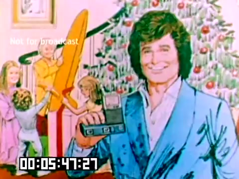 The still features a colorful illustration of a man wearing a light blue suit, holding a Kodak camera. He has a friendly smile and is standing in front of a Christmas tree adorned with decorations. Around him, children are engaged in playful activities, adding to the festive atmosphere. The bottom of the frame displays a timestamp indicating the position in the film. The overall aesthetic reflects the cheerful, promotional nature of a 1970s Kodak sales film, emphasizing family moments and holiday spirit.