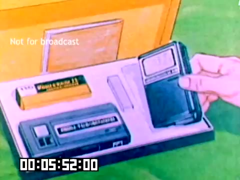 The still features a hand holding a compact camera, showcasing a neatly arranged set of Kodak products. Included in the display are a camera, a battery, and an accessory, likely a tape or storage device, all set against a vibrant green background. The text 'Not for broadcast' is visible, indicating the film's intended use. The bottom of the image has a timecode, suggesting it is part of a longer sequence.