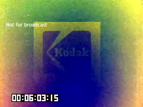 The still is a faded 16mm frame from a 1977 Kodak sales film. It features the iconic Kodak logo, partially visible and framed by a colorful, abstract overlay. The text 'Not for broadcast' appears in the upper left corner, indicating its restricted use. The timestamp at the bottom suggests the film's position within its runtime. Overall, the image conveys a vintage aesthetic reflective of the era's film quality.