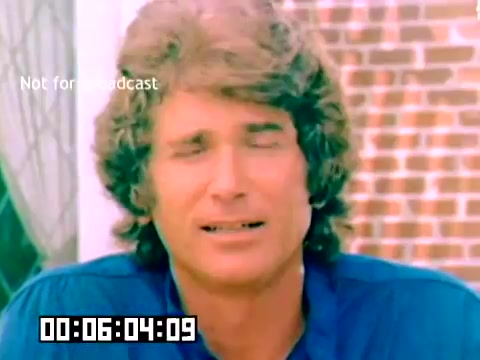 The still captures a close-up of a man with curly hair, expressing a serious demeanor. He wears a blue shirt and appears to be mid-sentence, possibly conveying a message or promoting a product. The background features a brick wall and some greenery, hinting at an informal setting. A timestamp at the bottom indicates a specific duration. The image is marked 'Not for broadcast,' emphasizing its private or restricted use.