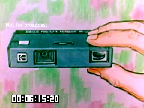 The 16mm still shows a hand holding a Kodak camera, illustrating the product in a promotional context. The camera appears compact, with distinct features like a lens and buttons. The background is colorful and abstract, possibly aimed at catching the viewer’s attention. A timestamp and 'Not for broadcast' are visible, indicating it's for internal use or demonstration only.