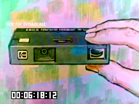 The still features a hand holding a Kodak camera, highlighting its design and branding. The camera appears to have a simple, sleek layout with identifiable Kodak logos. The background is colorful and abstract, adding a vintage aesthetic typical of the late 1970s. The timecode suggests it is part of a longer presentation, likely aimed at promoting Kodak's products.