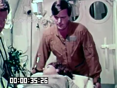 The still from the Air Force newsfilm 'Stopping gangrene - saving lives' depicts a medical scenario where a healthcare professional stands over a patient on a gurney. The setting appears to be a clinical or emergency environment, emphasizing the urgency of medical care. The focus seems to be on treating a serious condition, likely related to gangrene, highlighting the importance of rapid and effective medical intervention in life-threatening situations.