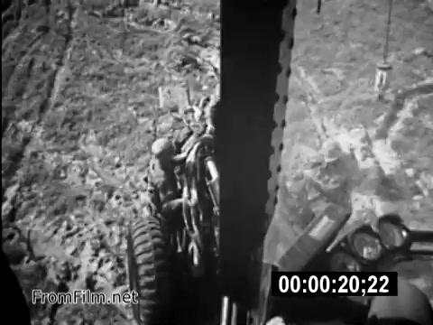 The still from 'Your Man In Vietnam' presents a view from inside a CH-54 helicopter cockpit, showcasing the daily operations of U.S. Army Specialist 6 James Daly as a flight engineer during the Vietnam War. The image captures equipment and a ground perspective, highlighting the rugged terrain and the complexities of military life in that era. This archival footage serves to inform the public about the realities faced by service members, emphasizing their commitment and the challenges of their roles.