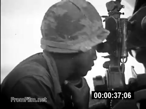 The still features a U.S. Army service member, wearing a standard military helmet, focusing intently as he operates a piece of equipment, likely a machine gun or targeting device. The background is cloudy, suggesting a tense atmosphere, reflective of the Vietnam War's challenges. This image highlights the daily realities and responsibilities faced by soldiers like Specialist 6 James Daly, emphasizing themes of duty and vigilance during the conflict.