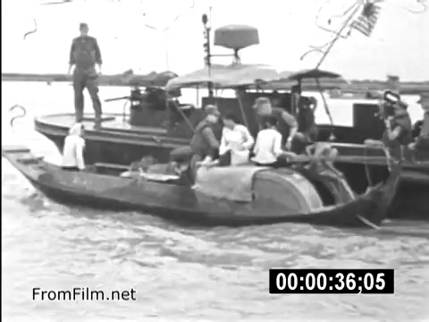 The still from 'Your Man In Vietnam' displays a scene on a river where a U.S. Army vessel is juxtaposed with a smaller boat. Soldiers are present on both boats, indicative of military operations and interactions in Vietnam. The image reflects the everyday realities faced by U.S. service members during the Vietnam War era, capturing the environment and challenges of military life. The presence of an American flag on the larger boat underscores the military context of the scene.