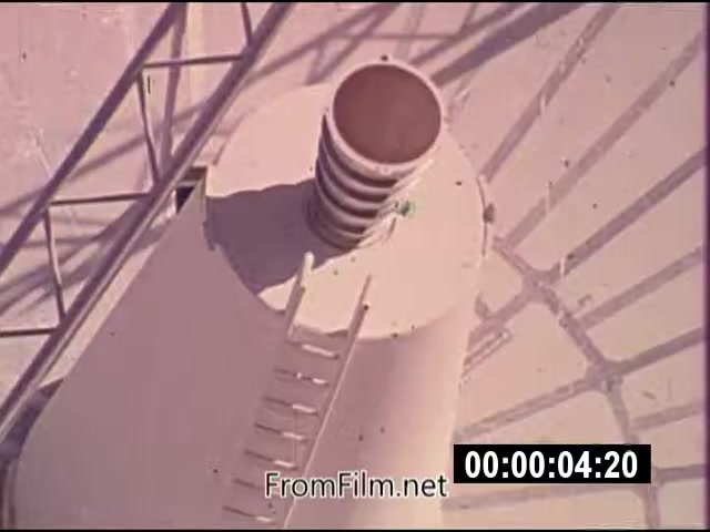 The 16mm still from 'Energy From Space' depicts a top-down view of a cylindrical structure, likely associated with energy transmission or satellite technology. It features a ribbed opening and a ladder leading up the side. The scene is washed in warm colors, hinting at a dusty or sunlit environment, and is part of NASA actuality footage from September 1976, emphasizing advancements in energy generation from space. The footage is silent and runs for 1 minute and 46 seconds.