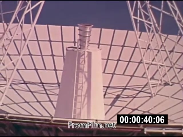 The still from 'Energy From Space' (1976) features a close-up view of a large parabolic dish structure, likely part of a satellite or solar energy system. Prominent are the metallic components above the dish, including a vertical chimney-like structure and a nearby ladder. The setting suggests an emphasis on technology related to harnessing energy from space. The film is silent, in color, and consists of actuality footage, indicative of NASA’s efforts in exploring energy solutions.