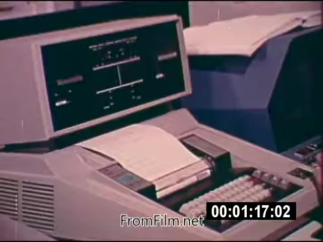 The still features a vintage 16mm film frame from NASA's 'Energy From Space,' dated September 1976. It showcases a portion of a technological apparatus, possibly a computer or data processing machine. The device displays various buttons, controls, and a screen, alongside printed materials. The context suggests this footage was part of a report sent to a West Virginia TV station, emphasizing advancements in space energy research at the time. The film is silent, presented in color, and runs for 1 minute and 46 seconds.