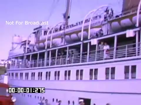 The still features a large ship docked with people visible on its decks. The ship, which appears to be a passenger vessel, has multiple decks and railings. There are individuals standing along the sides, some waving. In the foreground, a red vehicle is parked near the water's edge. The scene is captured in vibrant Kodachrome, giving it a lively, colorful appearance typical of mid-20th century footage. The labeling of 'Not For Broadcast' suggests it is for private or archival use.