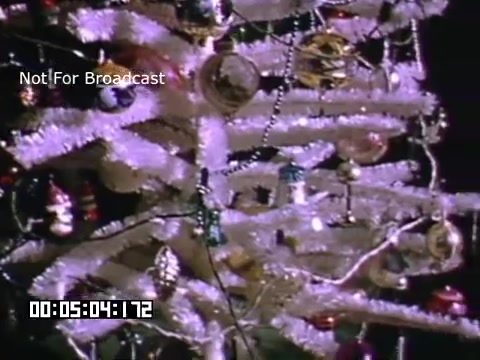 The still features a decorated Christmas tree, likely a retro-style aluminum or tinsel tree, adorned with shiny ornaments and beads. The bright colors of the decorations contrast against the metallic branches, creating a festive atmosphere. The visuals suggest a nostalgic holiday setting, likely captured in the mid-20th century, given the Kodachrome quality. The timestamp and 'Not For Broadcast' label indicate it's a preserved piece of film footage.