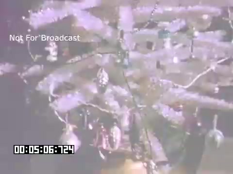 The still captures a vintage scene featuring a decorative Christmas tree, adorned with shiny ornaments and tinsel. The lighting creates a warm, nostalgic atmosphere typical of 1960s holiday celebrations. The tree likely symbolizes family gatherings and festive cheer, reflecting the time's cultural aesthetics. The inclusion of the digital timer at the bottom suggests it is a segment from a film, indicating a specific point in the footage.