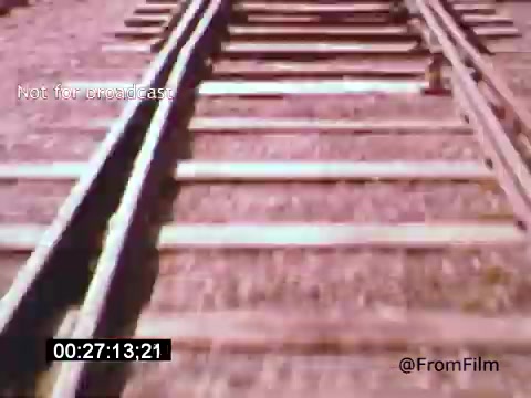 The still from 'Vincent Van Gogh: A Self-Portrait' (1961) depicts a close view of railway tracks. The wooden ties and metal rails form a stark, linear composition that leads the eye into the distance. The color tones are likely warm, typical of the film's era, adding a nostalgic feel to the image. This moment captures a sense of journey, which may reflect Van Gogh's tumultuous life and artistic explorations. Lee J. Cobb's narration likely adds depth to this visual storytelling.