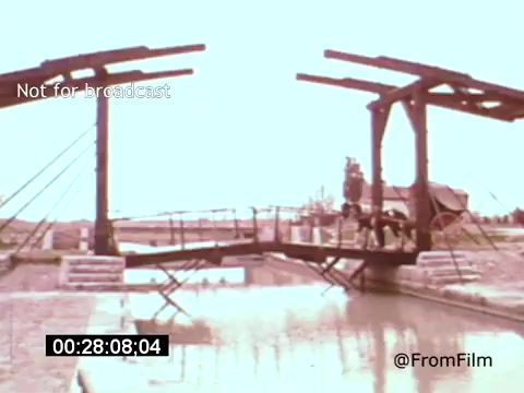 The still from 'Vincent Van Gogh: A Self-Portrait' (1961) features a picturesque scene with a wooden drawbridge spanning a tranquil waterway. The bridge, supported by strong wooden beams, is the focal point, while a horse-drawn wagon waits nearby. The muted colors and soft lighting evoke a serene, pastoral setting, reminiscent of Van Gogh's own artistic style and reflective of his life in the rural countryside. The overall composition suggests themes of labor and connection to nature, integral to Van Gogh's narrative.