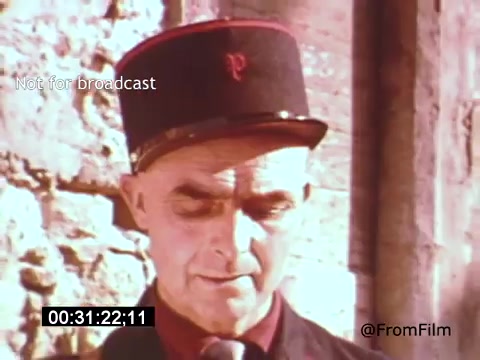 The still from 'Vincent Van Gogh: A Self-Portrait' (1961) features a man in a vintage uniform with a distinctive cap, adorned with a letter 'P.' The setting appears to be outdoors, possibly near a stone wall. The man's expression is pensive, creating a contemplative atmosphere that aligns with the film’s exploration of Van Gogh’s life and artistry. The scene captures a moment that may reflect on themes of identity and perception.