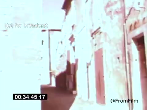 The still from 'Vincent Van Gogh: A Self-Portrait' (1961) features a sunlit street scene, likely depicting a quaint, old-world atmosphere. The buildings are textured and weathered, reflecting the historical context of Van Gogh's life. The color palette suggests a warm, nostalgic tone, enhancing the intimate portrayal of the artist's environment. Lee J. Cobb's narration adds depth to this visual representation of Van Gogh's world.