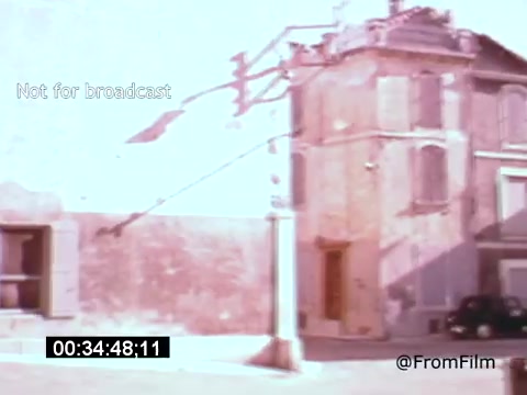 The still from 'Vincent Van Gogh: A Self-Portrait' (1961) features a muted, pastel-colored urban scene. It depicts a building with an overhanging roof and a streetlamp, suggesting a quiet, introspective atmosphere. A shadowy presence of vintage cars hints at the time period. The soft focus and faded colors evoke a sense of nostalgia, aligning with Van Gogh's artistic themes. The image is marked 'Not for broadcast,' indicating it is intended for archival purposes.