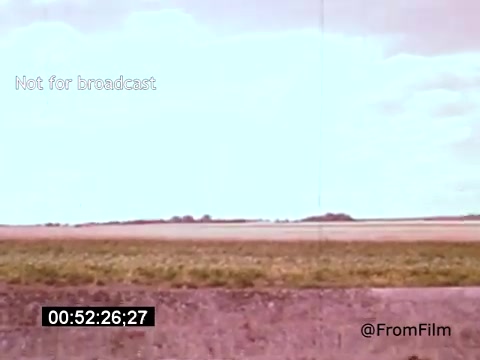 The still from 'Vincent Van Gogh: A Self-Portrait (1961)' features a wide landscape shot showcasing expansive fields under a cloudy sky. The colors have a washed-out quality, typical of 16mm film, evoking a sense of nostalgia. The scene captures a moment of tranquility, reflecting the essence of nature that Van Gogh often depicted in his works. The timestamp indicates it's part of a longer sequence in the film.