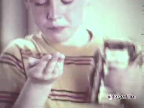The still shows a young boy with a striped shirt, focused on a handful of M&M's candies. He seems to be enjoying the treat, with a slight mess around his mouth, indicating excitement or indulgence. The nostalgic hues and soft focus reflect the 1960s aesthetic typical of animated commercials, which aimed to capture the joy of childhood and the fun of enjoying M&M's.