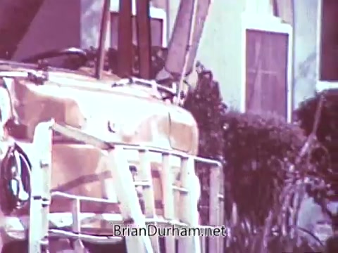 The still features a crane or a similar equipment, likely part of the setup for the Red Rose Tea commercial. The image captures a close-up view, showing structural details and possibly some foliage in the background. The overall tone suggests a vintage aesthetic, reflective of the production style in the late 1960s. The missed opportunity of processing the vibrant color footage in black and white adds a layer of nostalgia.