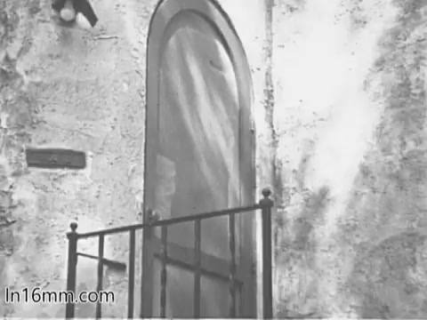 The still from the 'Give Heart Fund PSA - 1960's' features a close-up of a door with a screen and decorative ironwork. The door appears to be situated in an outdoor setting, possibly suggesting a home environment. The overall tone is vintage, capturing the essence of the era's public service announcements aimed at promoting heart health awareness. The simplicity of the image may evoke a sense of community and outreach.