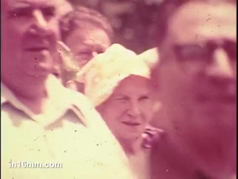 The still features a group of older adults, with a woman wearing a light-colored headscarf prominently in the foreground. The image captures a moment likely related to community engagement, reflecting the themes of senior citizens' issues. The colors are soft and slightly faded, typical of 16mm film from the 1970s. The expressions of the individuals suggest a gathering or event focused on the senior community.