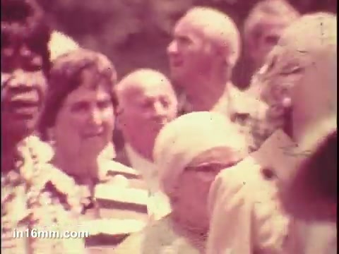 The still captures a group of seniors during a public service announcement in 1975. They appear engaged and attentive, set against a bright background. The image reflects a sense of community among older adults, emphasizing their visibility and presence in society. The colors and film quality are characteristic of the era, contributing to the nostalgic tone.