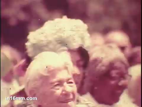 The still from the 1975 PSA for the National Council of Senior Citizens features a group of older adults, with a focus on a smiling woman in the foreground. The atmosphere appears joyful, highlighting a gathering or event aimed at seniors. The colors are soft, typical of the film style of that era.