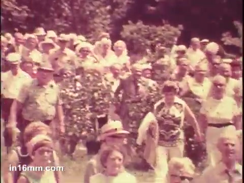 The still from the 'National Council of Senior Citizens PSA - 1975' features a large group of seniors walking together outdoors. The scene conveys a sense of community and engagement among older adults, highlighting their active participation. The vibrant surroundings and casual attire suggest a warm, sunny day, promoting a message of vitality and social involvement.