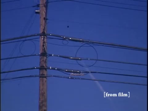 The still features a winter suburban street scene, showcasing power lines and a clear blue sky. The angle suggests a slight upward perspective, possibly emphasizing the intersection of urban infrastructure and residential life.