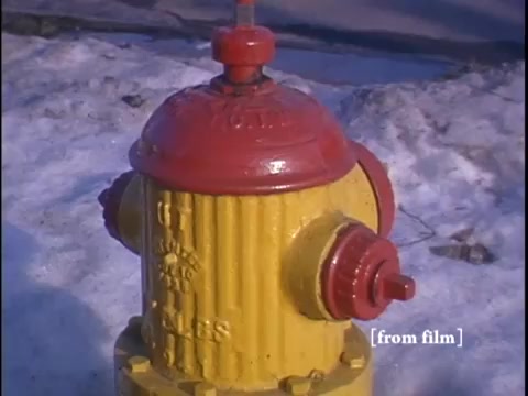 The still features a close-up of a yellow fire hydrant capped with a red lid, set against a backdrop of snowy ground typical of wintertime in a suburban neighborhood. The image captures a solitary moment in the street, emphasizing the everyday environment and subtle details of the era.
