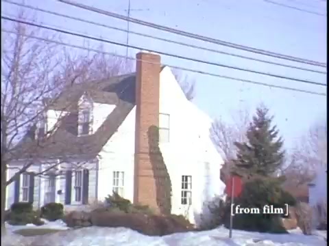 The film still captures a winter suburban street scene featuring a modest home with a prominent chimney, surrounded by snow and bare trees. In the foreground, a yellow fire hydrant adds a pop of color, while power lines stretch across the sky, conveying a quiet, everyday ambiance.