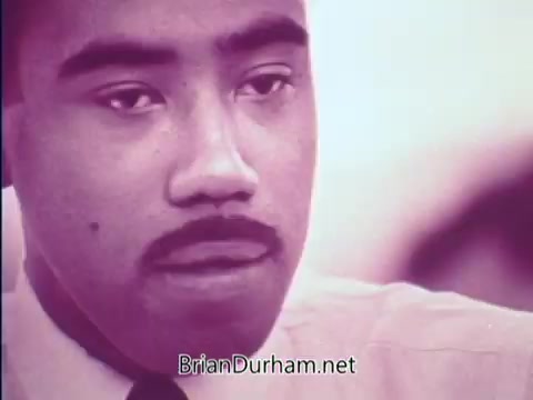 The still from the 1968 PSA 'Plans for Progress: Things Are Changing' features a close-up of a man with a thoughtful expression. The image is tinged with a pink hue, highlighting the intensity of his gaze. The context suggests themes of social change and advocacy during a pivotal era in American history. The focus on his face emphasizes personal reflection and engagement with the changing societal landscape.