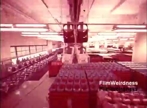 The still from 'Bell Performance' showcases a factory floor scene from the 1970s, emphasizing the manufacturing process of telephones. The environment is filled with rows of telephone components and assembly lines. The lighting has a warm, nostalgic hue, typical of the era's film, conveying a sense of industriousness and history in telecommunications. The equipment and layout reflect the period's technology and production methods used by the Bell System.